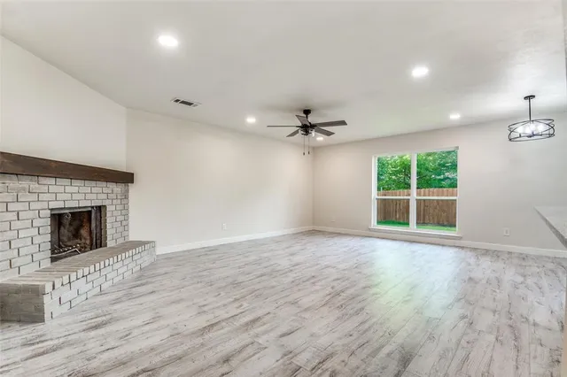 a view of an empty room with wooden floor fireplace and a window