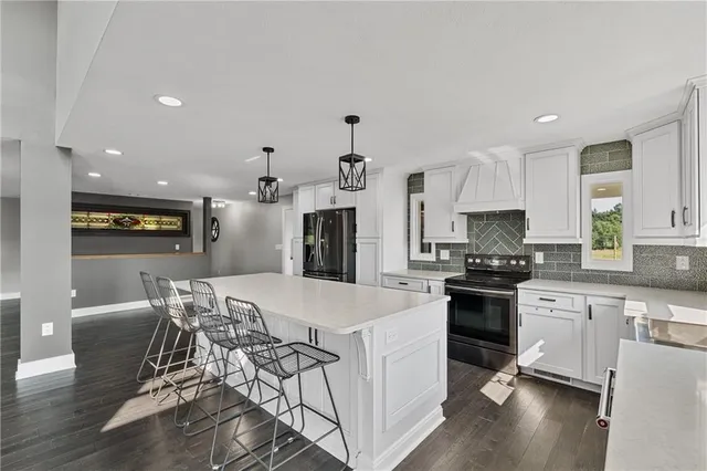 a kitchen with stainless steel appliances granite countertop a refrigerator a sink dishwasher a stove and white cabinets with wooden floor