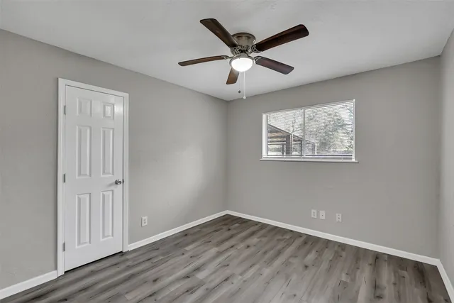 an empty room with wooden floor ceiling fan and windows
