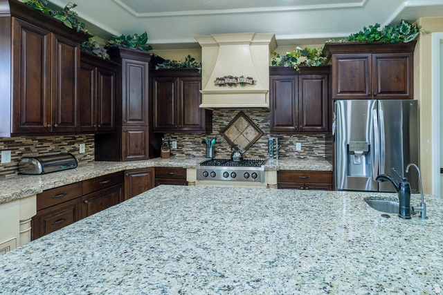 3683 South 2640 West St. George, UT 84790 - Photo 14 of 41 Spacious kitchen featuring a large island with an undermount sink, dark wood cabinetry, light-toned granite countertops, a tiled backsplash, and stainless steel appliances