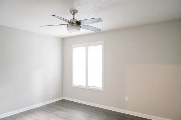 an empty room with wooden floor ceiling fan and windows