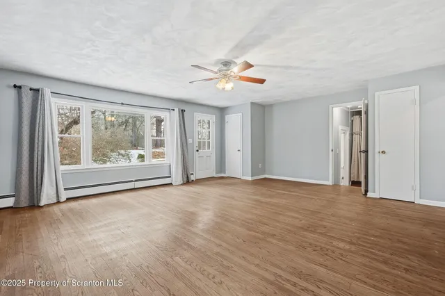 a view of an empty room with chandelier fan and wooden floor