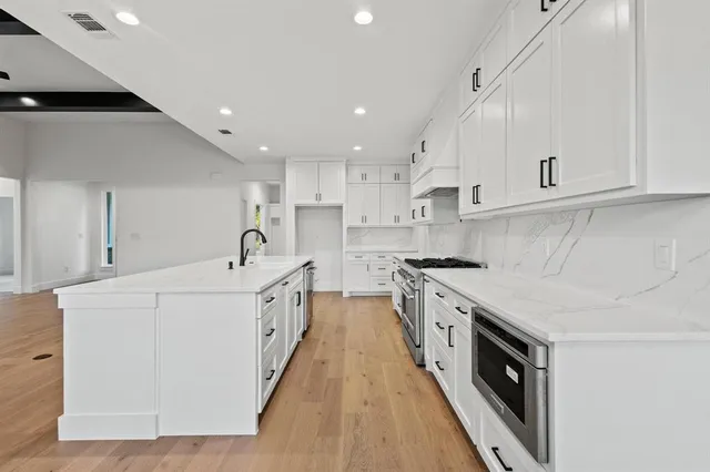 a large white kitchen with a stove a sink dishwasher and a refrigerator with wooden floor