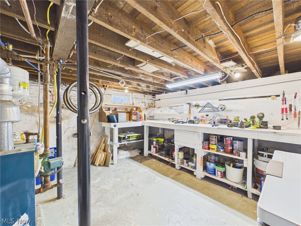 3490 County Line Road Madison, OH 44057 - Photo 37 of 42 Basement workshop featuring concrete flooring, exposed wood beams, a pegboard wall, built-in shelving, and a small transom window