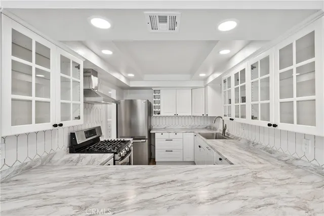 a large white kitchen with granite countertop a stove a sink a window and white cabinets