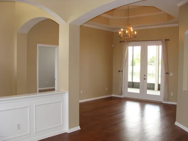 an empty room with wooden floor chandelier and windows