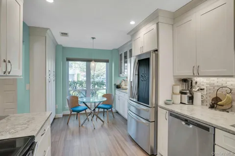 a kitchen with stainless steel appliances granite countertop a refrigerator a sink a stove and white cabinets with wooden floor