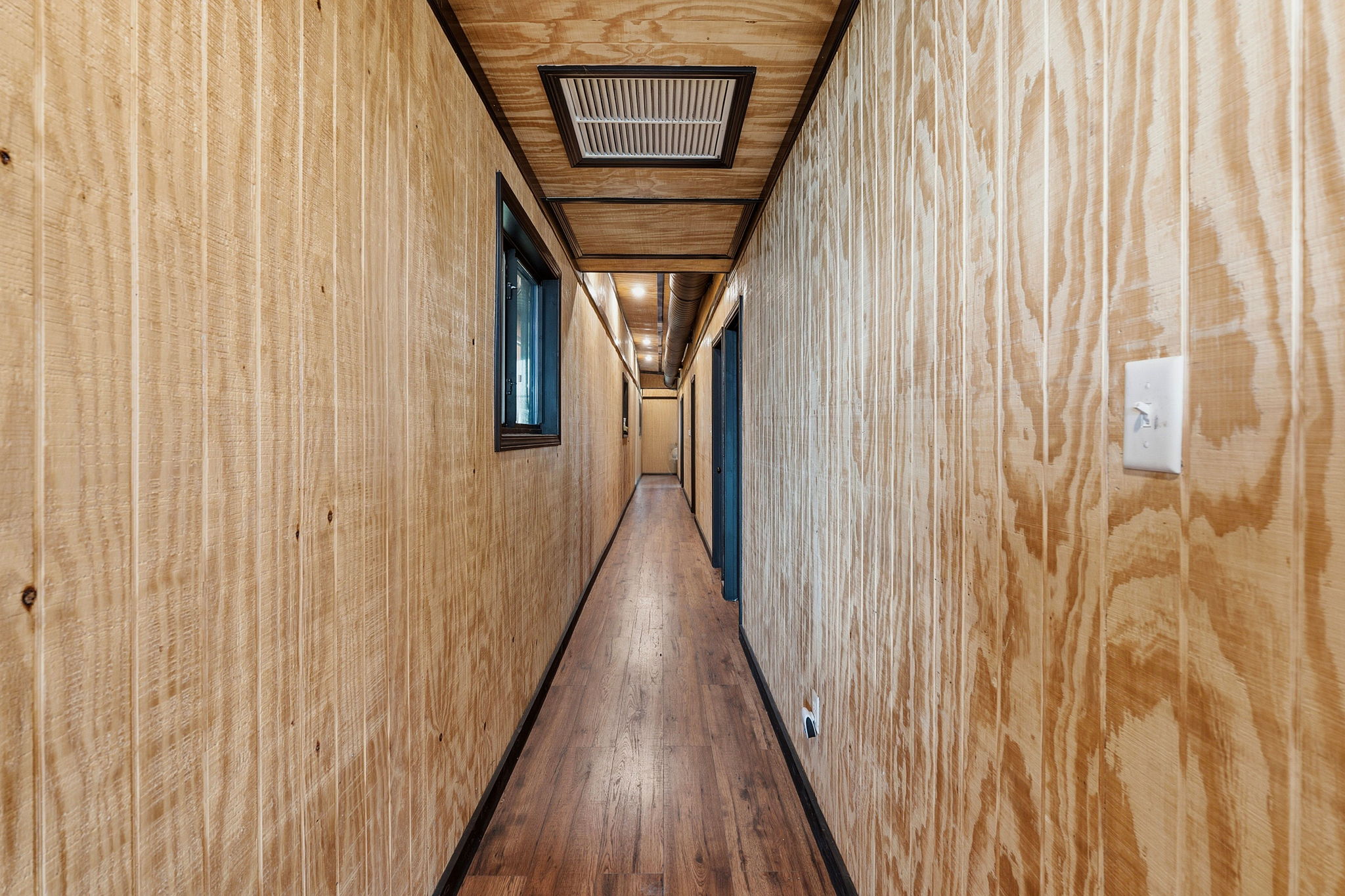 1701 County Road 466 Elgin, TX 78621 - Photo 5 of 24 A well-lit hallway with natural wood paneling and dark wood flooring extends towards multiple entryways.