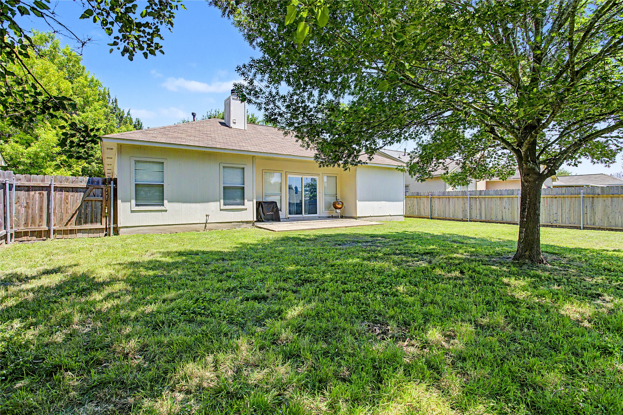 207 Kates Way Hutto, TX 78634 - Photo 21 of 24 Expansive fenced backyard featuring a mature shade tree, a concrete patio, and a light-toned exterior
