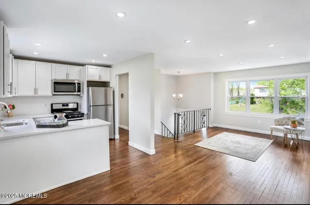 a kitchen with stainless steel appliances granite countertop a refrigerator a stove top oven a sink dishwasher and white cabinets with wooden floor