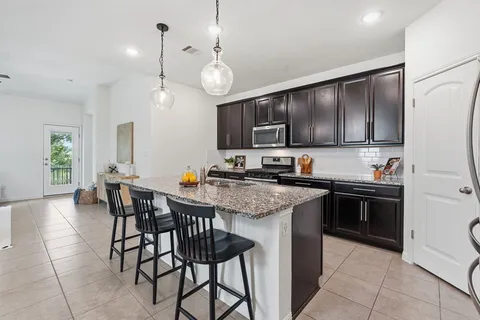 a kitchen with stainless steel appliances granite countertop a stove top oven a refrigerator a sink and chairs