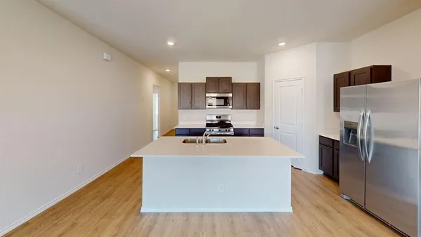 a view of a kitchen with kitchen island a sink wooden floor and stainless steel appliances