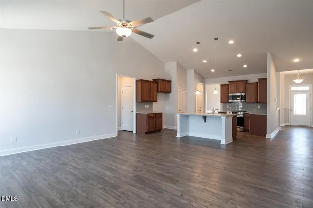 a view of an empty room and kitchen with ceiling fan