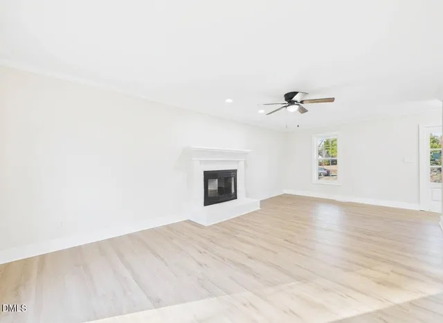 a view of an empty room with wooden floor and a ceiling fan