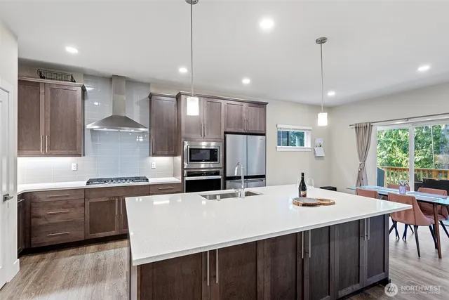 a kitchen with stainless steel appliances kitchen island granite countertop a sink a stove a refrigerator cabinets and a dining table with wooden floor
