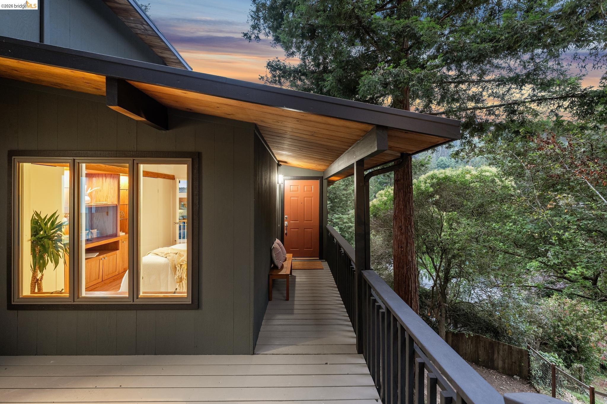 6645 Heather Ridge Way Oakland, CA 94611 - Photo 12 of 61 Exterior featuring a wood-paneled soffit, a covered entryway with a red door, a dark gray railing, and a window with a built-in wooden cabinet