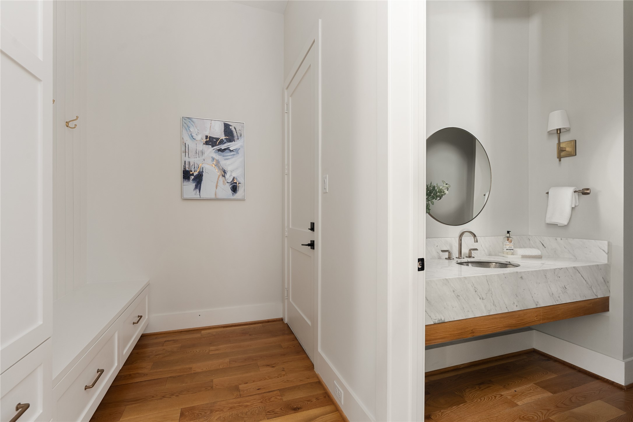 2715 Robinhood Street Houston, TX 77005 - Photo 17 of 48 A thoughtfully designed hallway and powder bath pairing showcases custom cabinetry, warm hardwood floors, and a marble vanity accented by refined brass fixtures for a cohesive, elevated look.