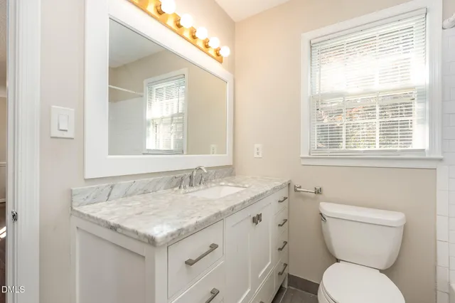 a bathroom with a granite countertop toilet a sink and a window