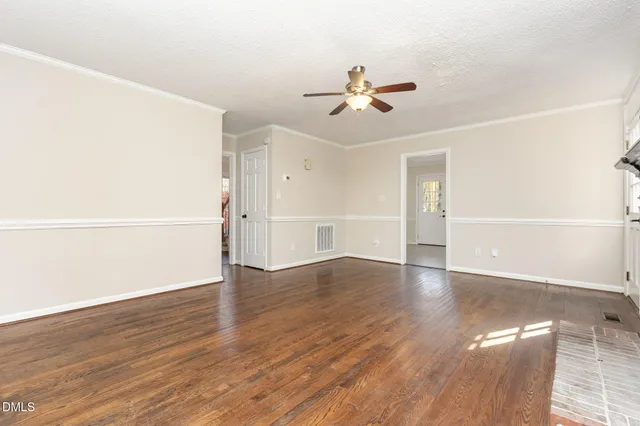 a view of an empty room with wooden floor and a ceiling fan