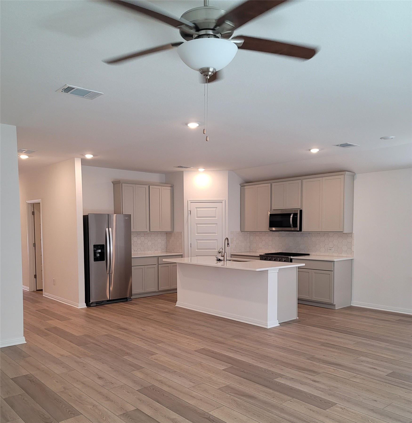 200 Callahan Loop Buda, TX 78610 - Photo 3 of 13 Open-concept kitchen featuring an island with a sink, stainless steel appliances, light gray cabinetry, and patterned tile backsplash
