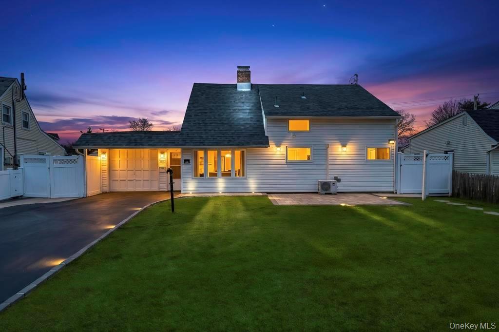 63 Blacksmith Road Levittown, NY 11756 - Photo 1 of 25 Back of house at dusk featuring a gate, an attached garage, asphalt driveway, a chimney, and a patio