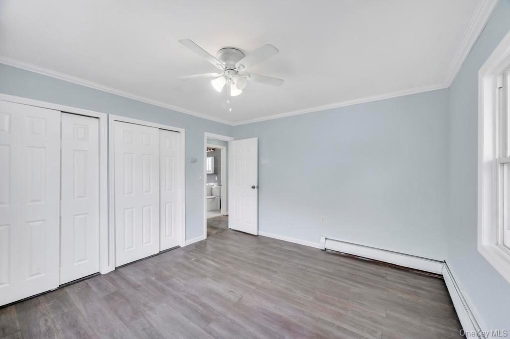 63 Blacksmith Road Levittown, NY 11756 - Photo 13 of 25 Unfurnished bedroom with multiple closets, ornamental molding, a baseboard radiator, light wood-type flooring, and a ceiling fan