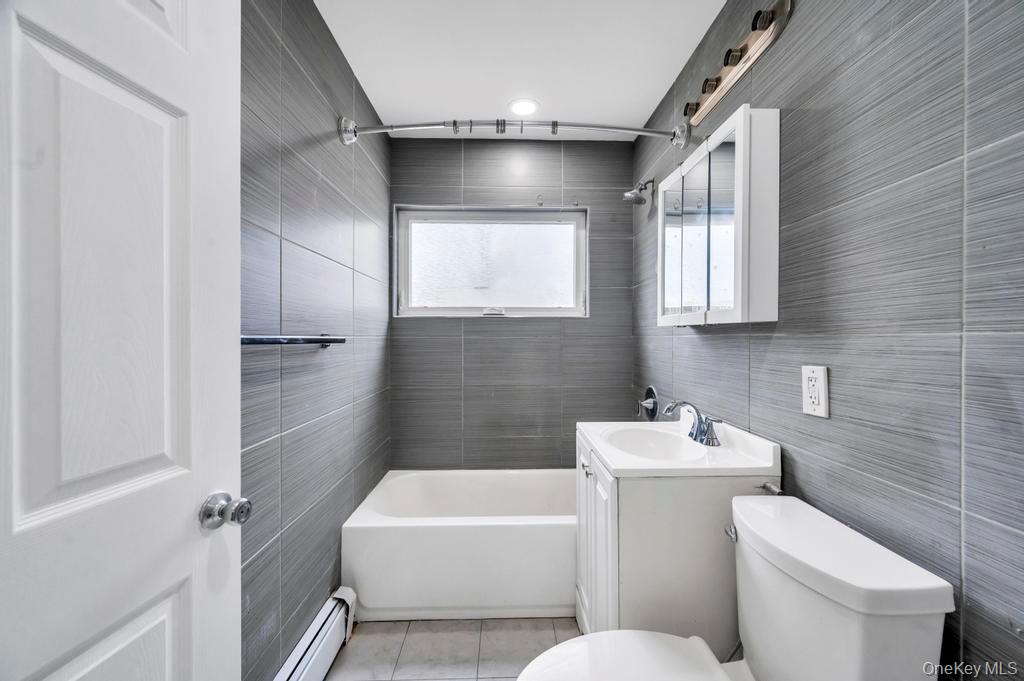 63 Blacksmith Road Levittown, NY 11756 - Photo 14 of 25 Full bathroom featuring tile walls, vanity, baseboard heating, shower / washtub combination, and light tile patterned floors