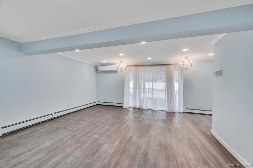 63 Blacksmith Road Levittown, NY 11756 - Photo 6 of 25 Empty room featuring baseboard heating, crown molding, light wood-type flooring, a baseboard radiator, and a chandelier