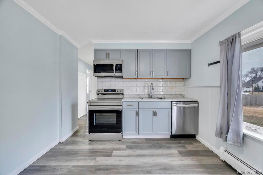 63 Blacksmith Road Levittown, NY 11756 - Photo 8 of 25 Kitchen with light countertops, stainless steel appliances, a baseboard radiator, gray cabinetry, and light wood finished floors