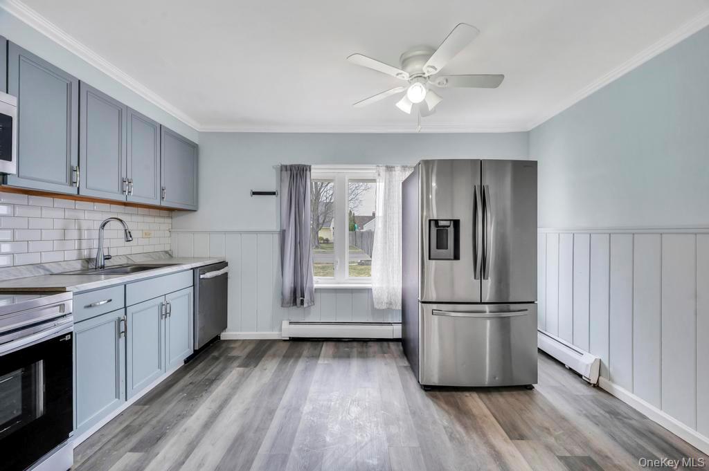 63 Blacksmith Road Levittown, NY 11756 - Photo 9 of 25 Kitchen featuring stainless steel appliances, light countertops, baseboard heating, gray cabinetry, and ornamental molding