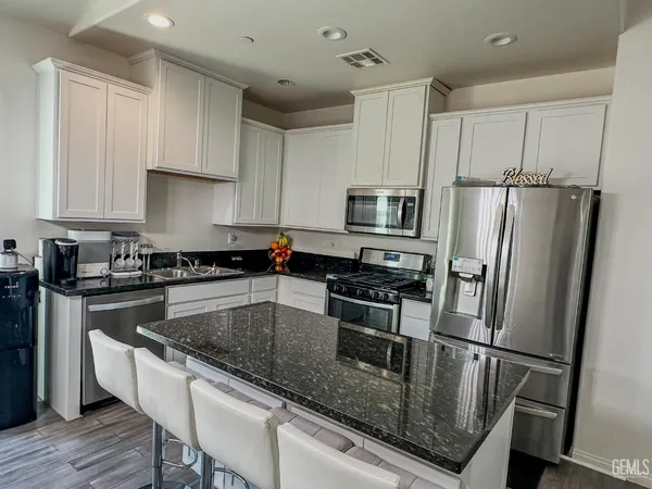 a kitchen with stainless steel appliances granite countertop a refrigerator a stove a sink a microwave and white cabinets