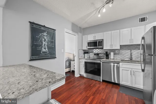 a kitchen with stainless steel appliances granite countertop a stove top oven a sink a refrigerator white cabinets and wooden floor