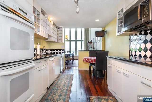 a kitchen with granite countertop a stove a sink and white cabinets with wooden floor