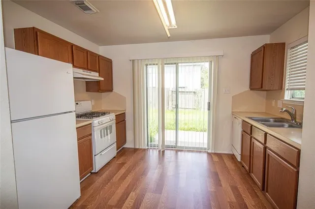 a kitchen with granite countertop a refrigerator a sink dishwasher stove and white cabinets with wooden floor