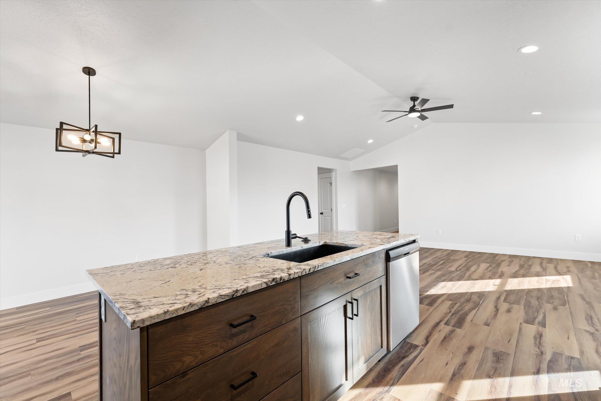 1142 Velvet Loop Wilder, ID 83676 - Photo 27 of 27 Kitchen featuring dark wood finish cabinetry, light wood-style floors, open floor plan, light stone countertops, and stainless steel dishwasher