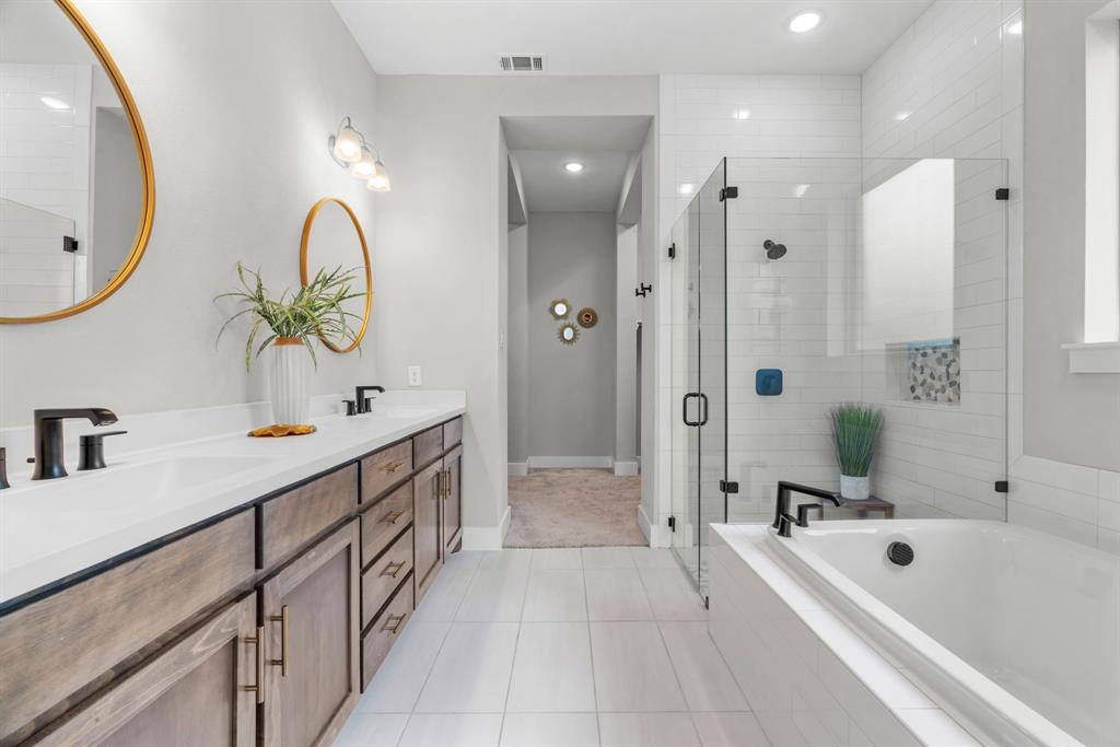 1821 Stonewall Road Argyle, TX 76226 - Photo 18 of 40 Spacious bathroom featuring a dual vanity with wood-finish cabinetry, a large soaking tub, a glass-enclosed shower with subway tile surround, and contemporary matte black fixtures