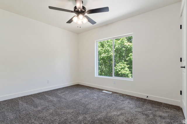 504 North 650 E Street Springville, UT 84663 - Photo 21 of 36 Neutral interior with a window featuring green foliage, dark gray patterned carpeting, white baseboards, and a ceiling fan with light fixture