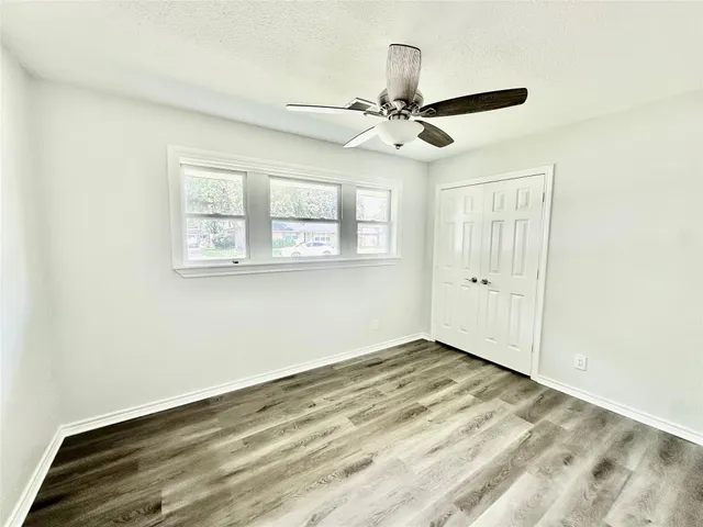 an empty room with wooden floor fan and windows