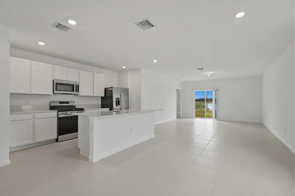 a large white kitchen with white cabinets a sink a stove a microwave a counter top and a refrigerator