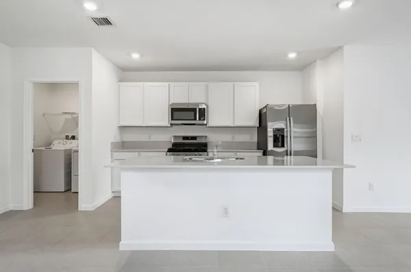 a large kitchen with stainless steel appliances granite countertop a stove a refrigerator a sink a microwave and white cabinets with wooden floor