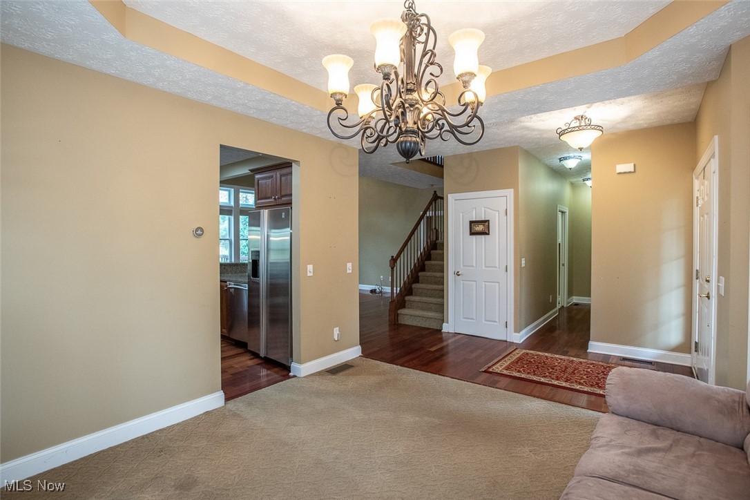 630 Rundle Street Lagrange, OH 44050 - Photo 6 of 49 Unfurnished living room featuring a textured ceiling, a tray ceiling, a chandelier, dark wood-style floors, and stairs