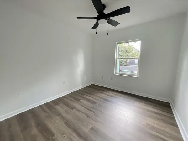 an empty room with wooden floor fan and windows
