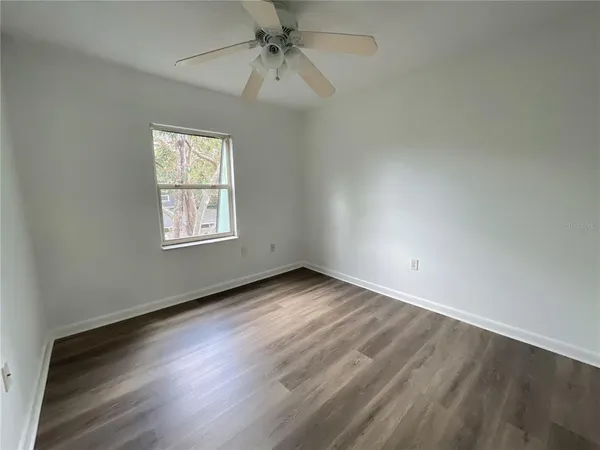 an empty room with wooden floor chandelier fan and windows
