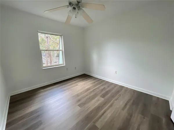 an empty room with wooden floor fan and windows