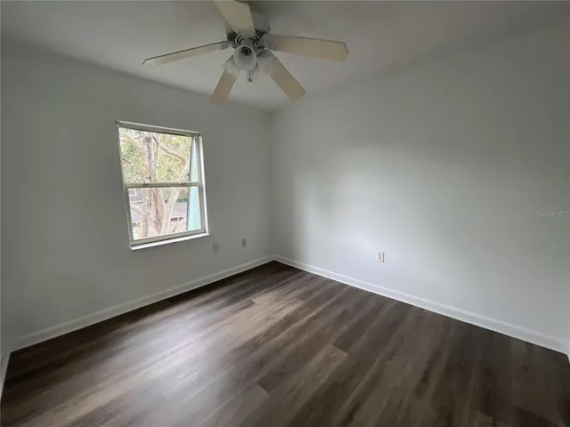 an empty room with wooden floor fan and windows
