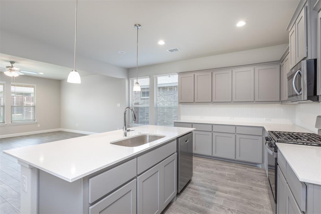 14621 Bootes Drive Haslet, TX 76052 - Photo 16 of 40 Kitchen with stainless steel appliances, gray cabinets, light wood-style flooring, hanging light fixtures, and a kitchen island with sink