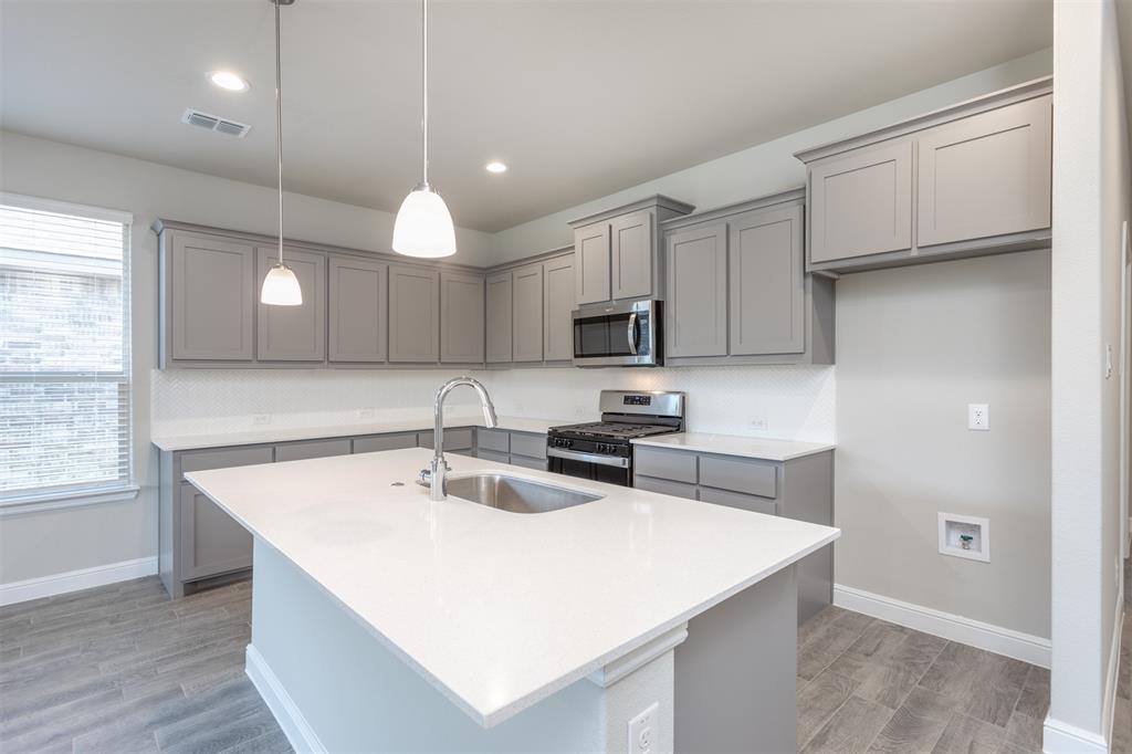 14621 Bootes Drive Haslet, TX 76052 - Photo 17 of 40 Kitchen with gray cabinets, stainless steel appliances, an island with sink, pendant lighting, and light stone counters