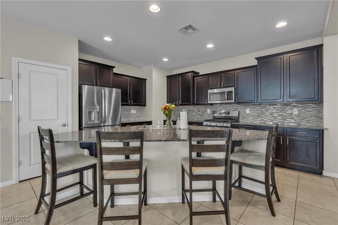 9950 Coyote Echo Court Las Vegas, NV 89166 - Photo 7 of 71 Kitchen featuring appliances with stainless steel finishes, light tile patterned flooring, a breakfast bar, dark stone countertops, and recessed lighting