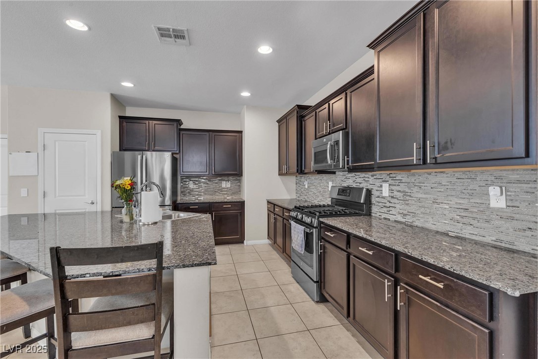 9950 Coyote Echo Court Las Vegas, NV 89166 - Photo 9 of 71 Kitchen with stainless steel appliances, dark brown cabinets, dark stone counters, light tile patterned flooring, and a breakfast bar area