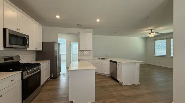 a kitchen with granite countertop a stove top oven a sink dishwasher a refrigerator and white cabinets with wooden floor